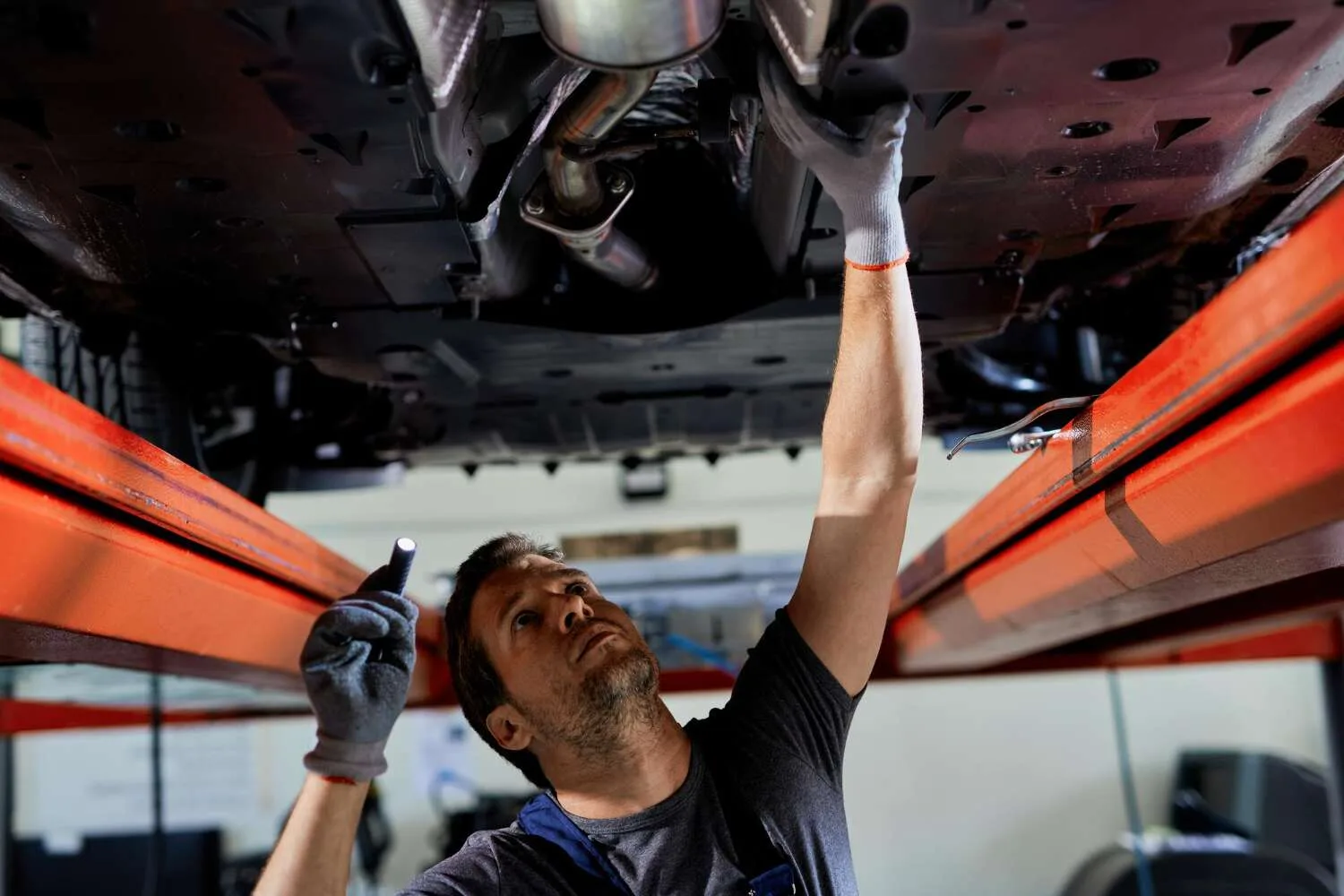 Mechanic inspecting car exhaust system under lift during noise check-up in Kuwait.