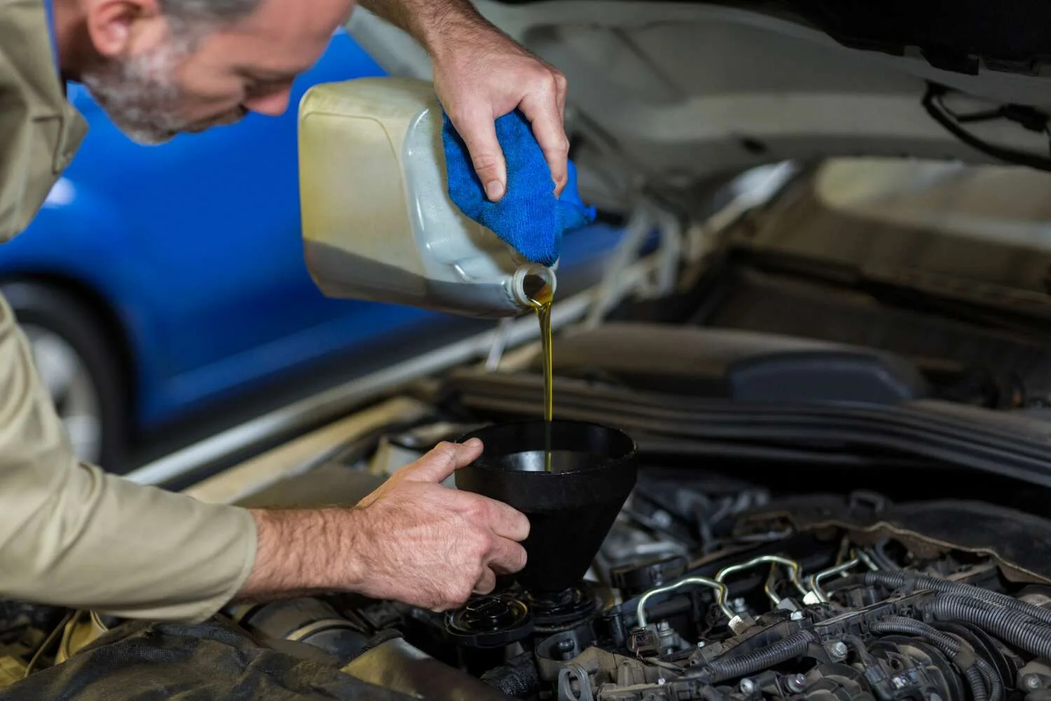 Mechanic performing car engine oil change service with funnel in Kuwait auto repair workshop.