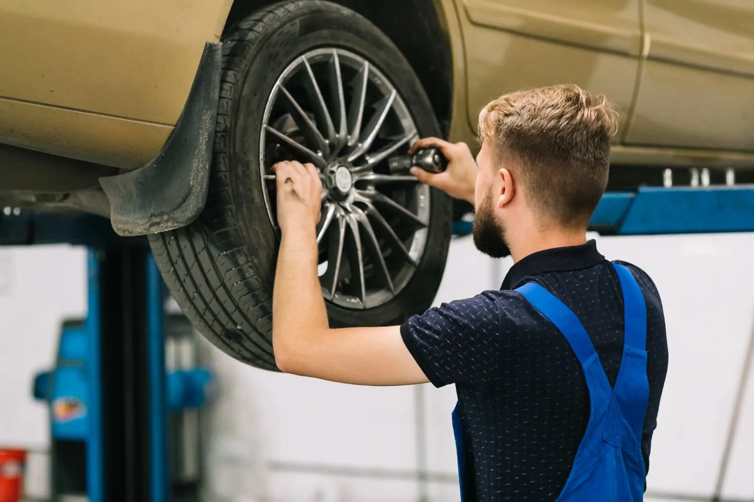  Mechanic performing wheel alignment service on car tire in Kuwait auto workshop.